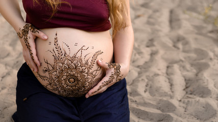 Pregnant belly with mehendi henna tattoo on the beach, cropped image, copy space