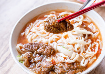 Beef noodle - Taiwan ramen meal with tomato sauce broth in bowl on bright wooden table, famous chinese style food, close up, top view, copy space