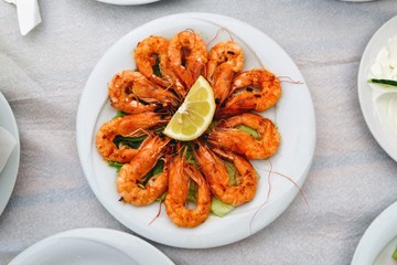 Delicious roasted shrimps with lemon on the plate. Fried seafood around quarter of a lemon on the restaurant table. Close up. Top view