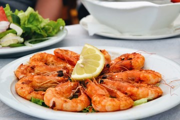Delicious roasted shrimps with lemon on the plate. Fried seafood around quarter of a lemon on the restaurant table. Close up