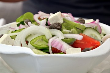 Delicious Greek salad in a bowl. Salad made of cucumber, tomato, pepper, lettuce, onion, feta cheese and olives. Concept for a tasty and healthy vegetarian meal. Healthy food. Close up