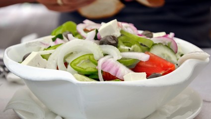 Delicious Greek salad in a bowl. Salad made of cucumber, tomato, pepper, lettuce, onion, feta cheese and olives. Concept for a tasty and healthy vegetarian meal. Healthy food. Close up, panoramic view