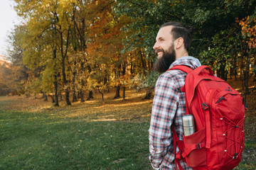 Autumn tourism. Portrait of happy hipster guy hiking with backpack in nature park. Fall landscape background.