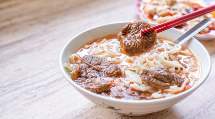 Beef noodle - Taiwan ramen meal with tomato sauce broth in bowl on bright wooden table, famous chinese style food, close up, top view, copy space