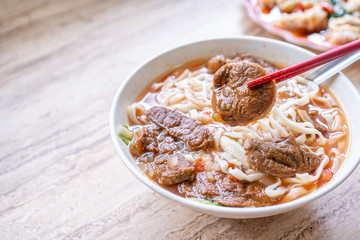 Beef noodle - Taiwan ramen meal with tomato sauce broth in bowl on bright wooden table, famous chinese style food, close up, top view, copy space
