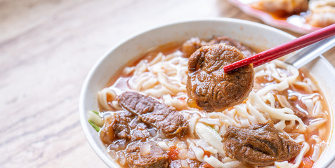 Beef noodle - Taiwan ramen meal with tomato sauce broth in bowl on bright wooden table, famous chinese style food, close up, top view, copy space