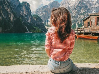 Fototapeta na wymiar Girl with long hair in striped shirt in the background of Lake Lago di Braies in the Dolomites, South Tyrol, Italy. Pier with romantic old wooden rowing boats on the lake. Amazing view of lake Lago di