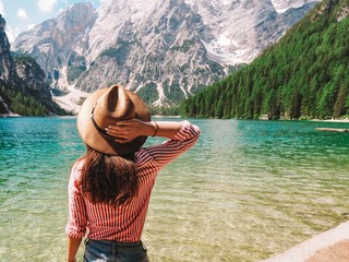 The girl with long hair wearing a wide-brimmed hat and a shirt striped on a background of Lake Lago di Braies in the Dolomites, South Tyrol, Italy. Pier with romantic old wooden rowing boats 