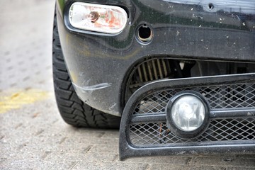 Road accident.  Black car with a broken bumper. Crushed automobile bumper. Parked auto with breakdown bumps and headlight. Car vandalism. 