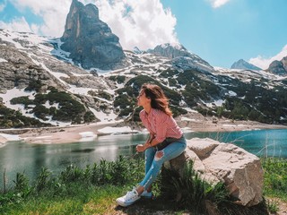 Naklejka premium A brunette girl with long hair fluttering in the wind stands against the background of the Dolomite mountains. Mountain summer landscape in the Dolomites in Northern Italy.