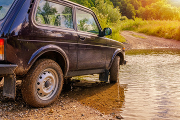 Off-road vehicle at a ford across the river in the glowing light of sunrise.
