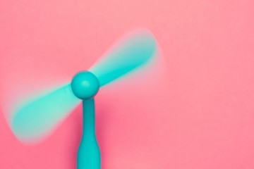 A small blue hand (usb) fan rotates on pink background with space for text