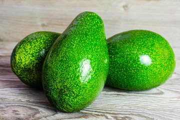 Three whole fruits of green avocado on wooden background. A juicy green avocado on a wooden kitchen table. Healthy tropical fruits.