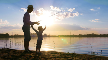 Father and son fishing on the river bank in the rays of sunset