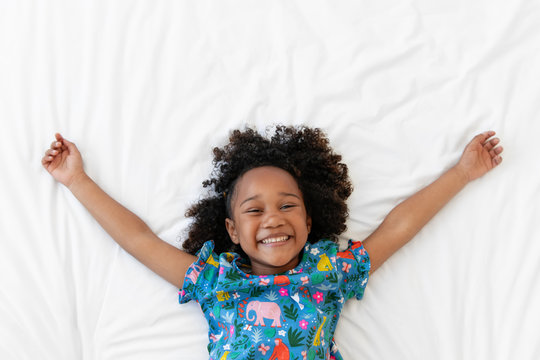 Happy little girl smiling on white bed with arms up