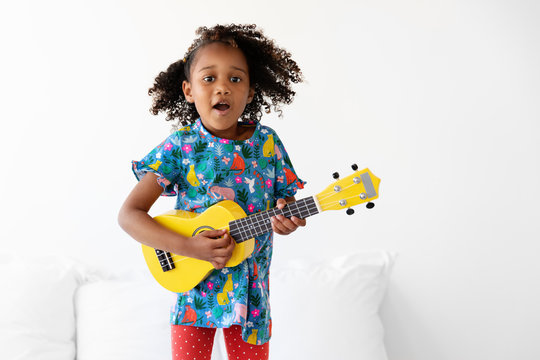 Portrait of young girl dancing on bed while playing the guitar