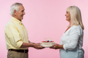 happy senior couple with grey hair holding birthday cake isolated on pink