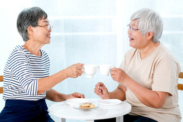 Two Asian elderly women drink tea together in the morning and also have some cookies, they are smile and talk about some stories.