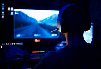 Shot of the Beautiful Pro Gamer Girl Playing in First-Person Shooter Online Video Game on Her Personal Computer. Casual Cute Geek wearing Glasses and Headset. Neon Room. eSport Cyber Games Internet © Катя Датунова