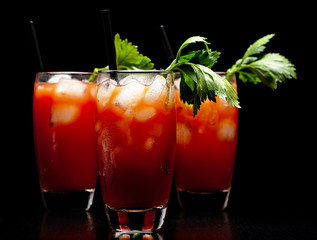 Red Bloody Mary drinks with ice cubes with celery isolated on black