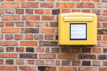 yellow german mailbox on brick wall