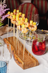 Assortment of canapes on wooden board. Banquet service with different food snacks and appetizers. Catering food, snacks with shrimp and pineapple iIsolated on white background. Party food.