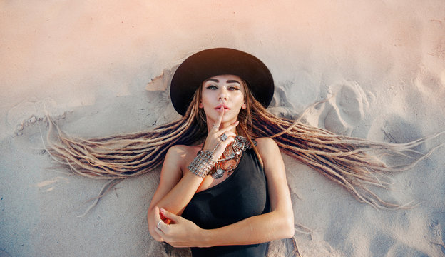 Girl with dreadlocks lying on the sand in a hat