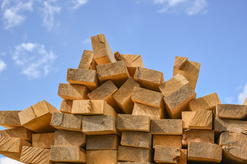 Stacked lumber on blue sky.Folded wood.Closeup wooden boards.The surface of the end of the board.Lots of planks stacked on top of each other in the warehouse.Lumber for use in construction.