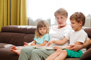 Grandmother with two child grandsons  having a great time  and reading a book at home. Family Reading Leisure 