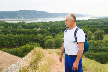 Naklejka na ściany i meble elderly man with backpack on the mountain. Senior man walking in nature. travel tourism concept