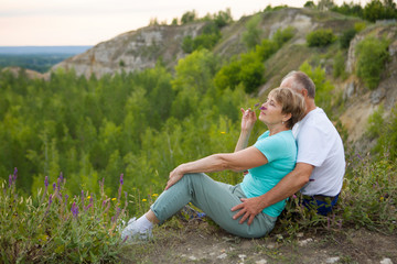 elderly couple sits on the mountain at sunset. Senior couple walking in nature. travel tourism concept