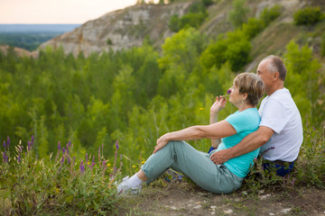 Fototapeta premium elderly couple sits on the mountain at sunset. Senior couple walking in nature. travel tourism concept