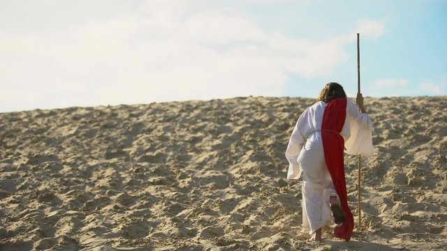 Hermit with staff walking in desert turning to camera, asceticism and fasting