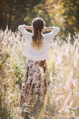 Back view of young romantic woman in white sweater walking on the autumn field.