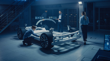 Team of Automotive Engineers Working on Electric Car Platform Chassis, Taking Measures, working...