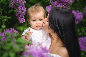 Mother kisses her daughter near a blossoming lilac. Purple colour. Spring image