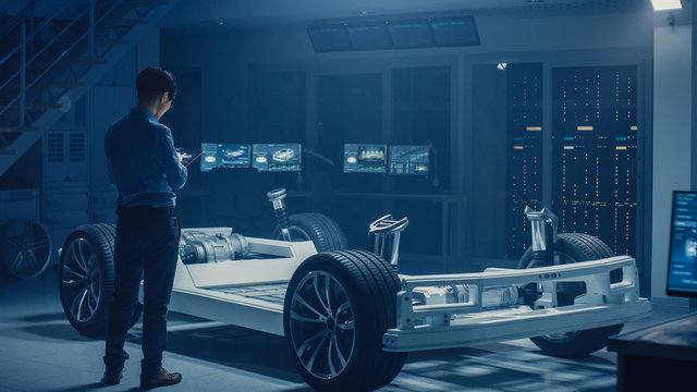 Automobile Engineer Working on Electric Car Chassis Platform, Using Tablet Computer Augmented Reality with 3D CAD Software Modelling. Innovative Facility: Vehicle Frame with Wheels, Engine, Battery