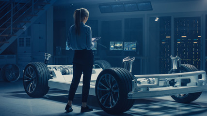 Automobile Female Engineer Working on Electric Car Chassis Prototype, Using Tablet Computer...