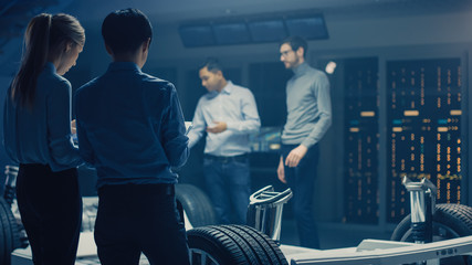 Automobile Engineers Discussing and Designing Electric Car Chassis Platform, Using Tablet Computers...