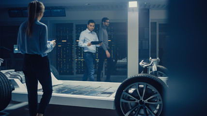Team of Automotive Engineers Working on Electric Car Chassis Platform, Taking Measures, working...