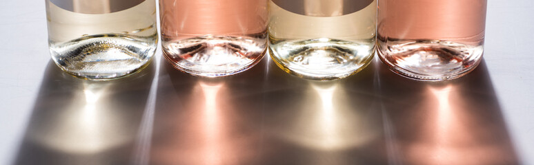 close up view of bottles with rose and white wine in row and back light, panoramic shot
