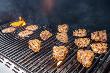 hot summer outdoor gas grill with hamburgers and lamb chops cooling with flames