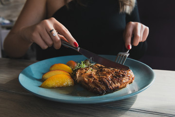 Girl cuts juicy grilled turkey steak with knife and fork on the turquoise plate. Chicken fillet. Steak served with caramelized peach.