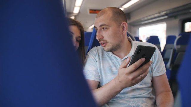 A couple in love traveling in the train, sitting in comfortable chairs looking at the photos on the smartphone.