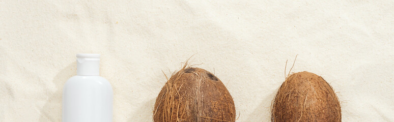 top view of coconuts and white sunscreen lotion on sand, panoramic shot