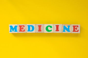The word "medicine" from wooden cubes. Letters on a yellow background. The concept of medicine and health.