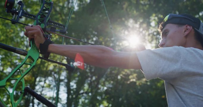 Slow motion close up of young man with professional equipment is practising archery with a bow in a woods in a sunny day. 
