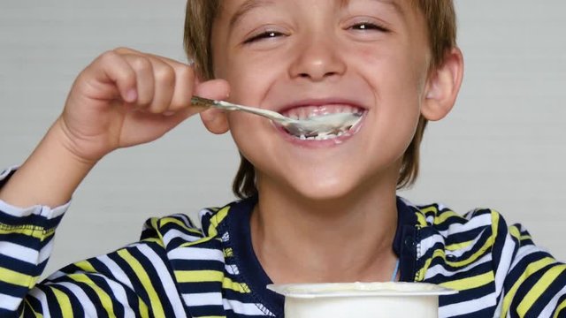 Cute boy European appearance is yogurt. Portrait of a happy child sitting at the table. Ecco, baby food.