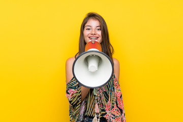 Caucasian girl in colorful dress over isolated yellow background shouting through a megaphone