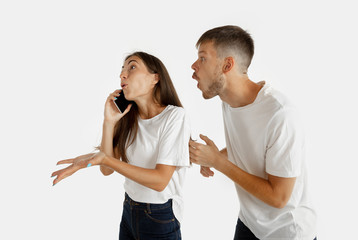 Beautiful young couple's portrait isolated on white studio background. Facial expression, human emotions, advertising concept. Woman talking on the phone, man wants to pay her attention on hisself.